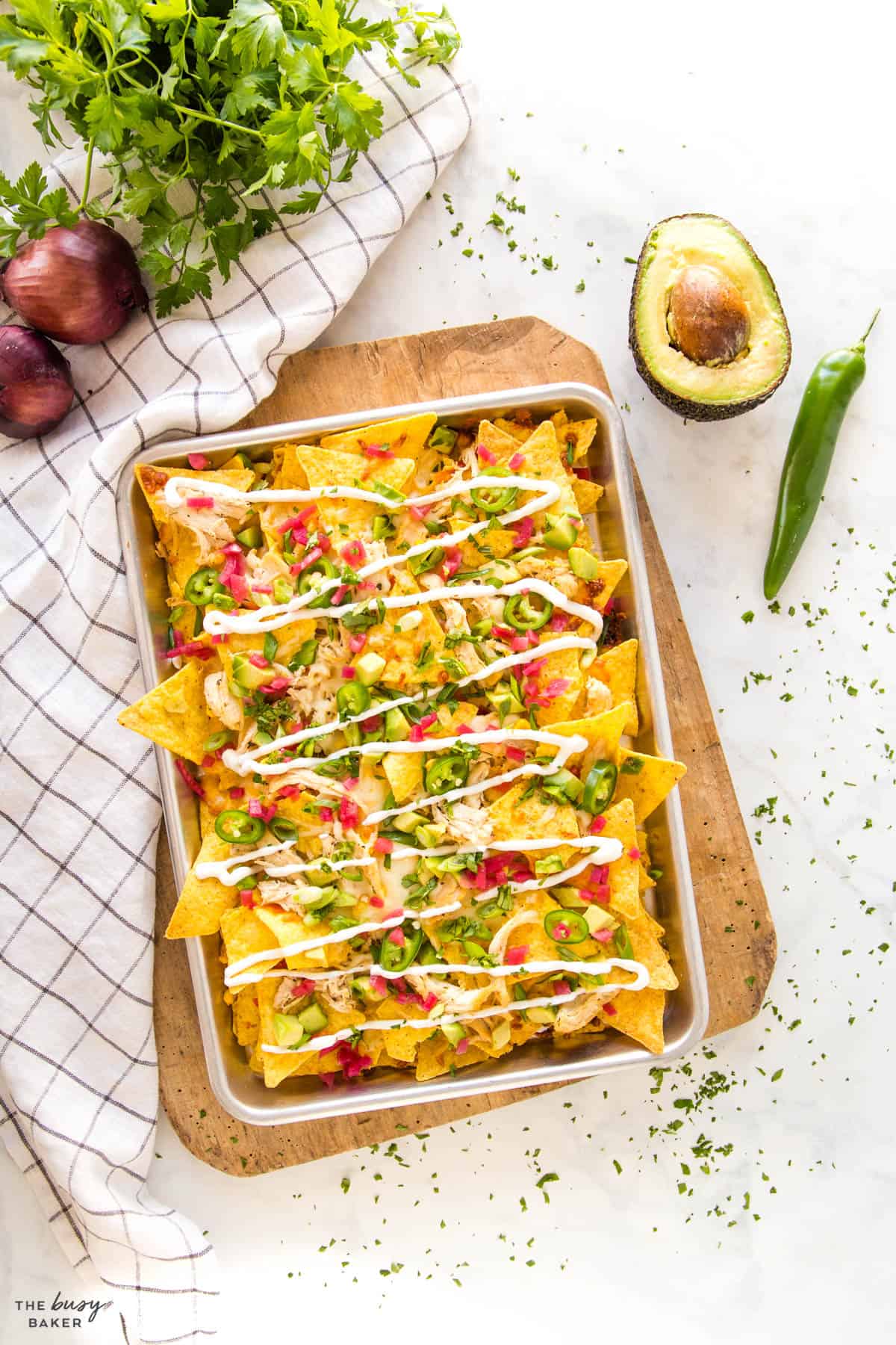 overhead image: sheet pan with chicken nachos, sliced avocado and a whole jalapeno 