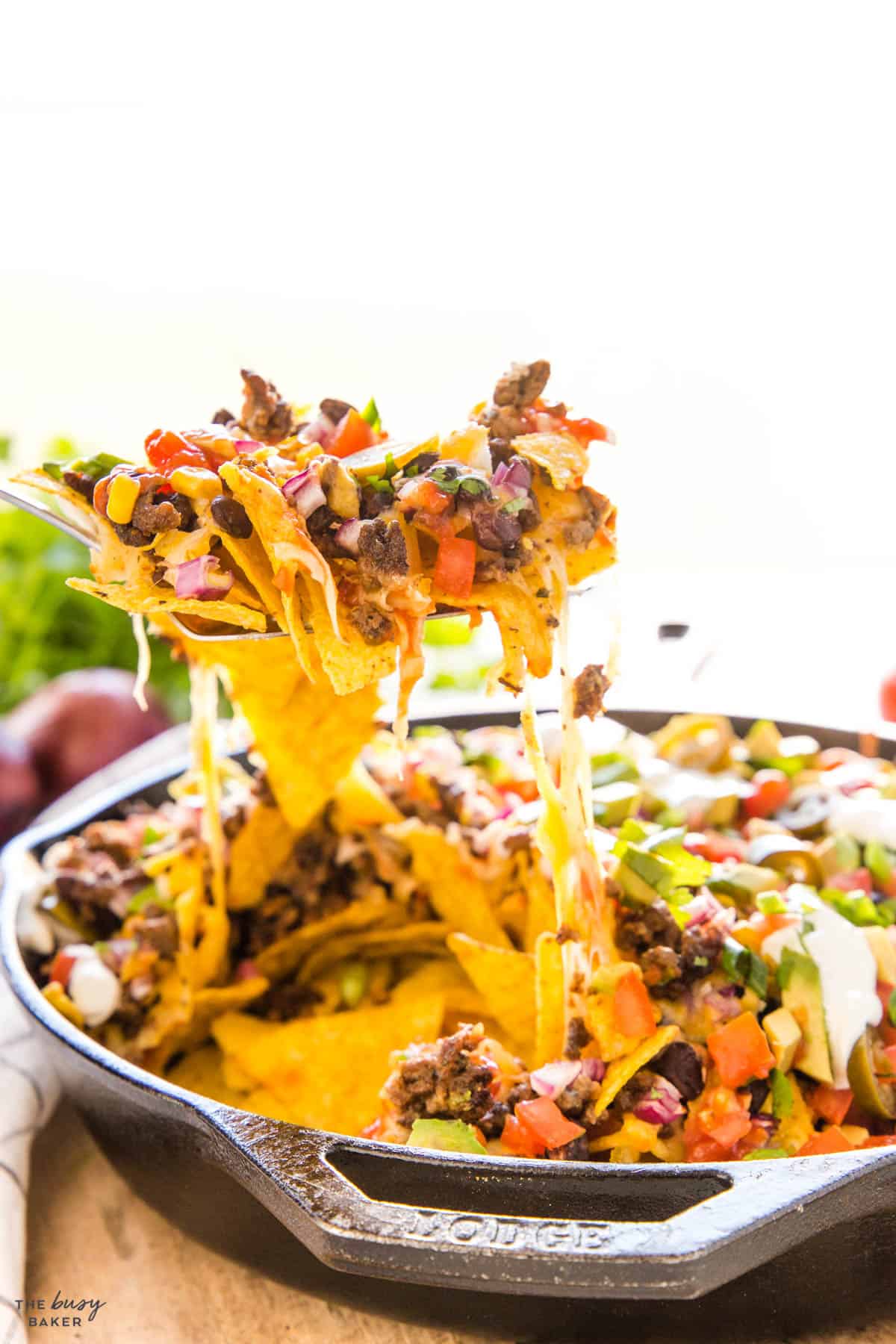close up image of loaded nachos on a fork above the cast iron pan.