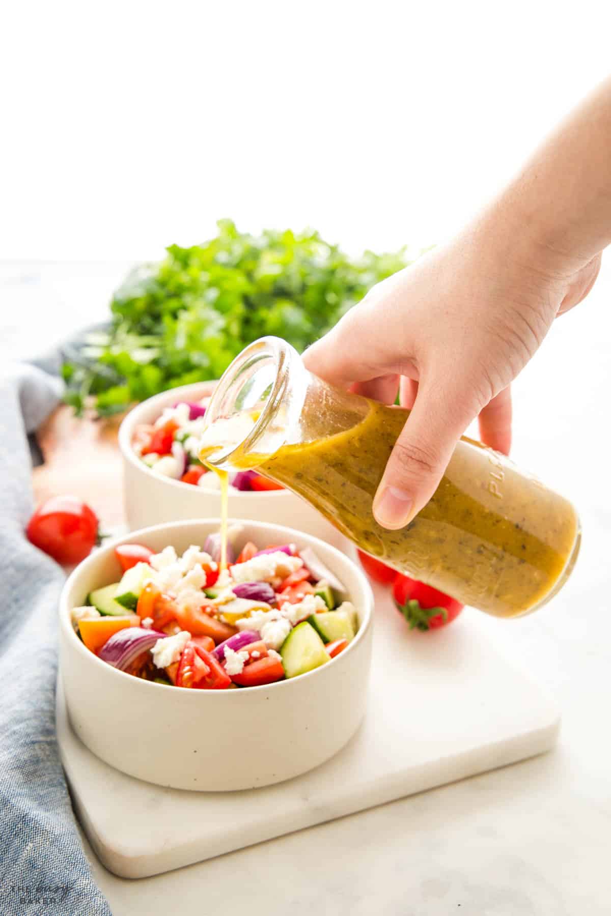 Greek salad dressing being poured over a Greek salad