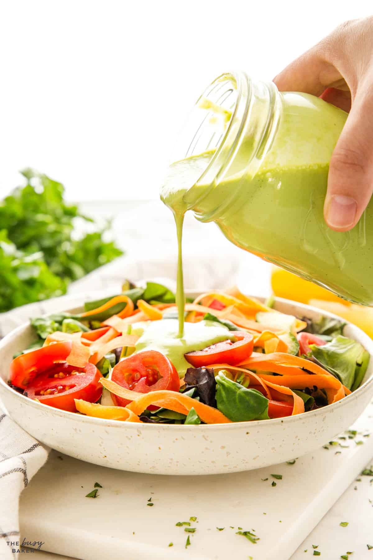 hand pouring creamy dressing over salad