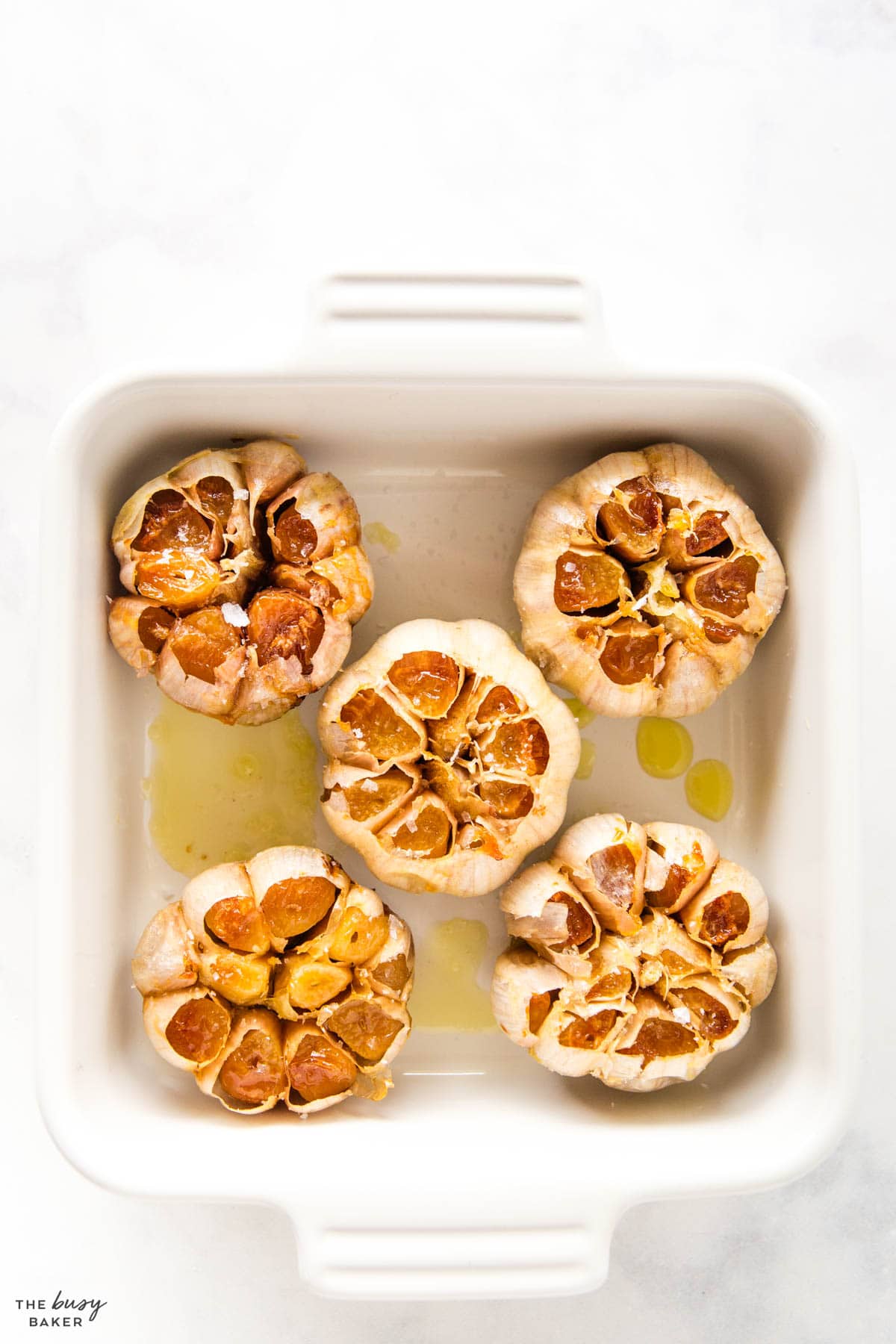 overhead image: roasted garlic in the oven a baking dish with olive oil and salt