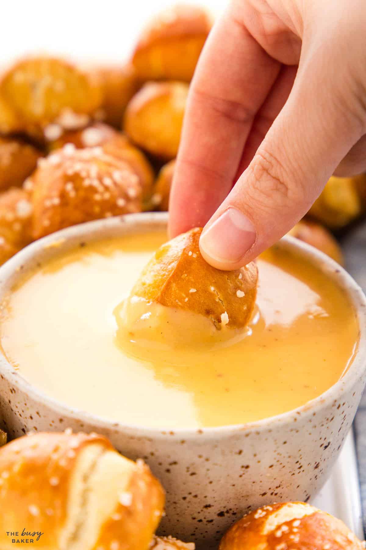 hand dipping a pretzel in homemade cheese sauce