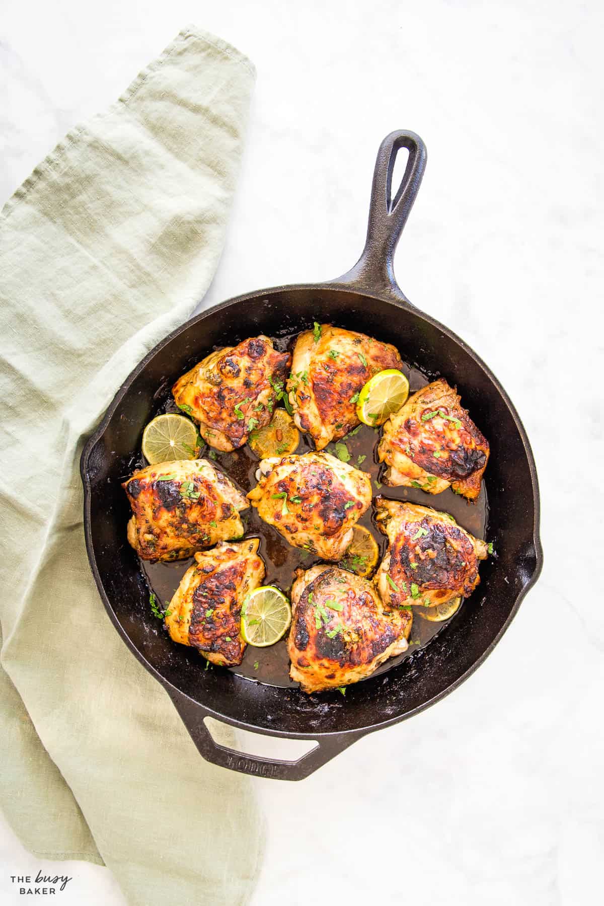 overhead image: chicken thighs with cilantro and lime in a cast iron skillet