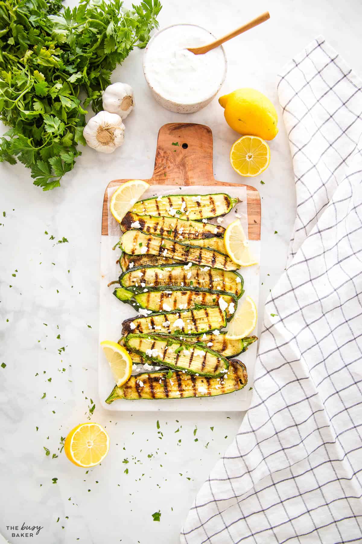 overhead image: grilled zucchini on a platter with lemon slices and feta