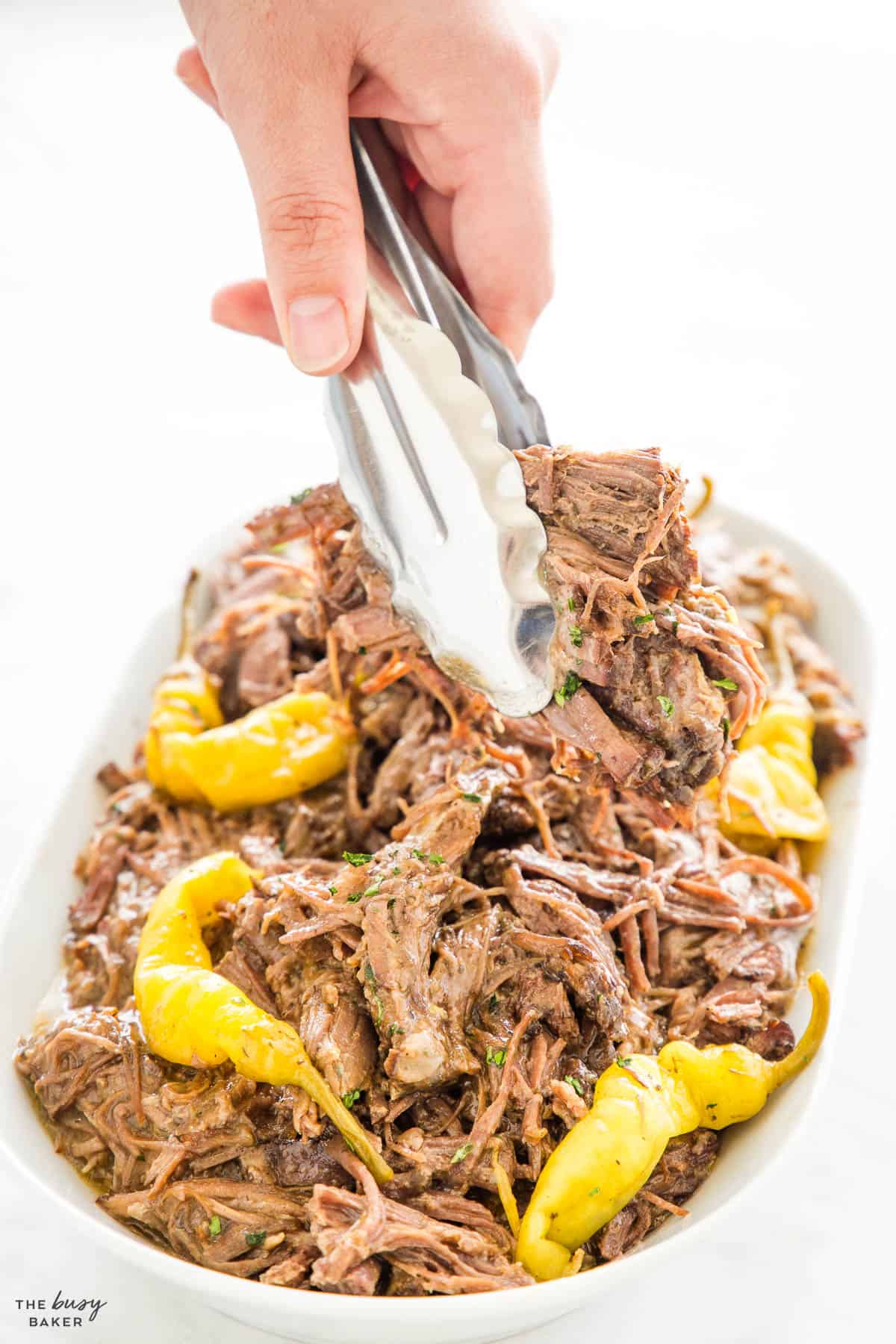 hand serving shredded beef with a pair of tongs
