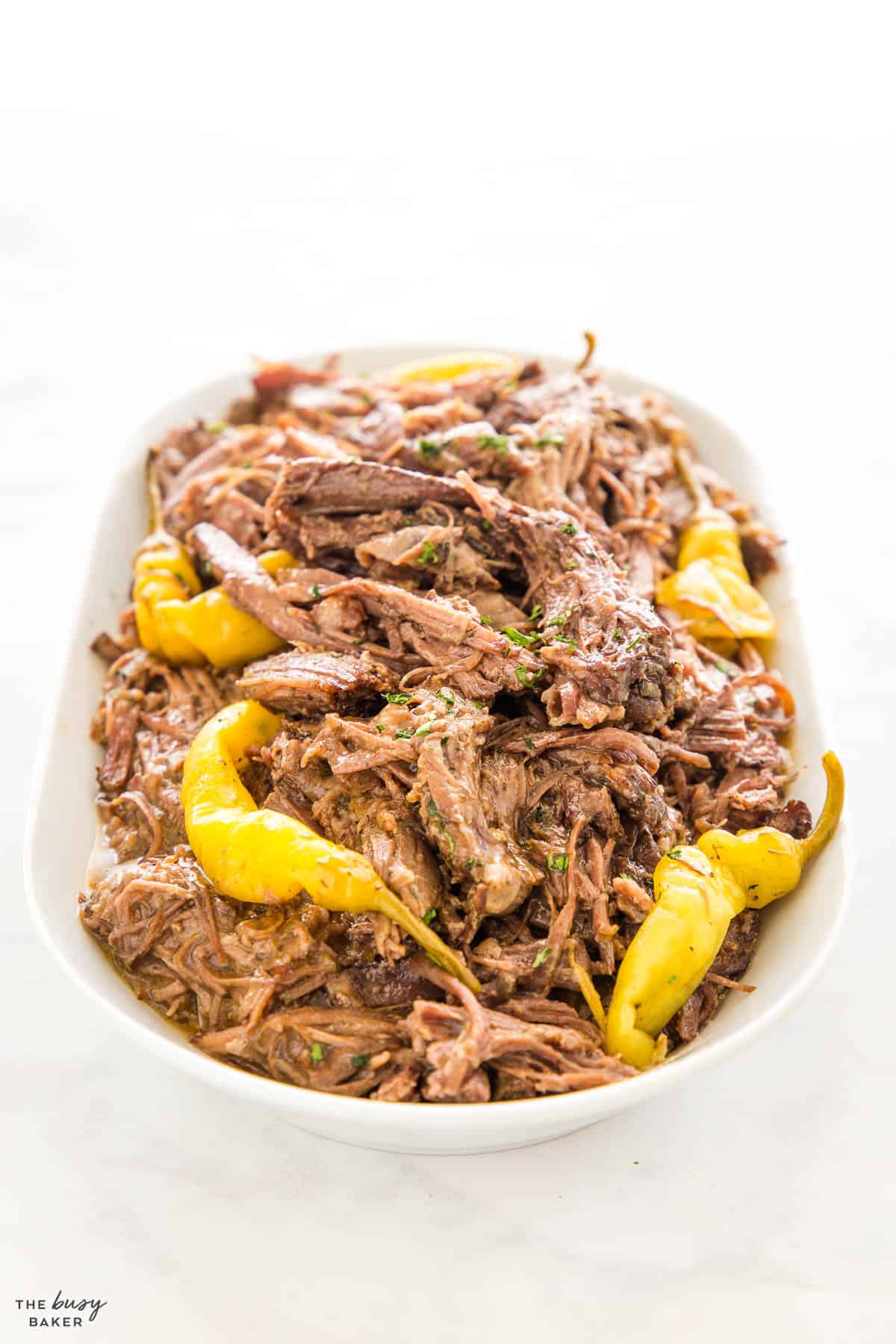 shredded beef on a white platter with pepperoncini peppers