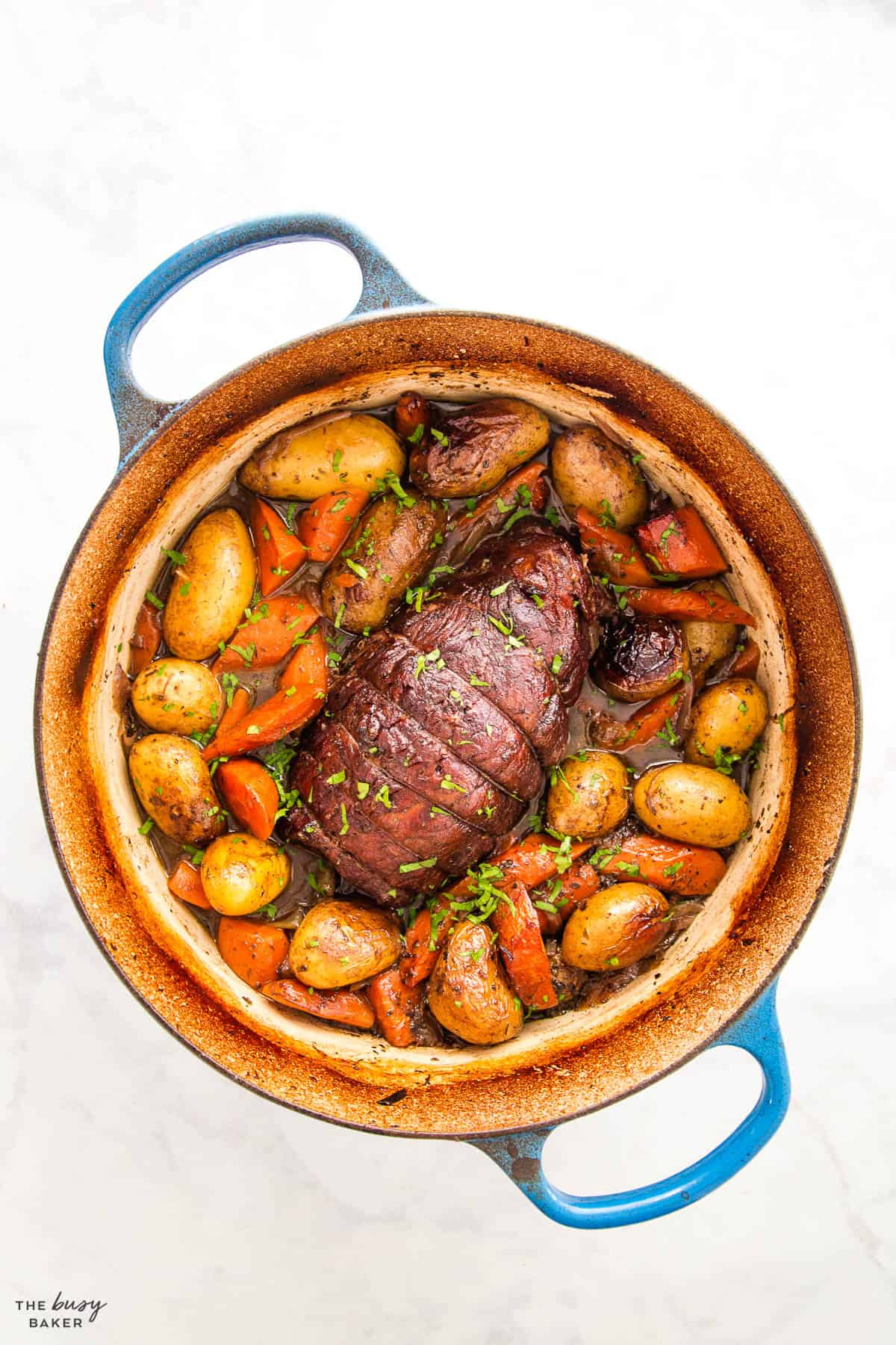 beef round roast in a blue pot with gravy, potatoes and carrots