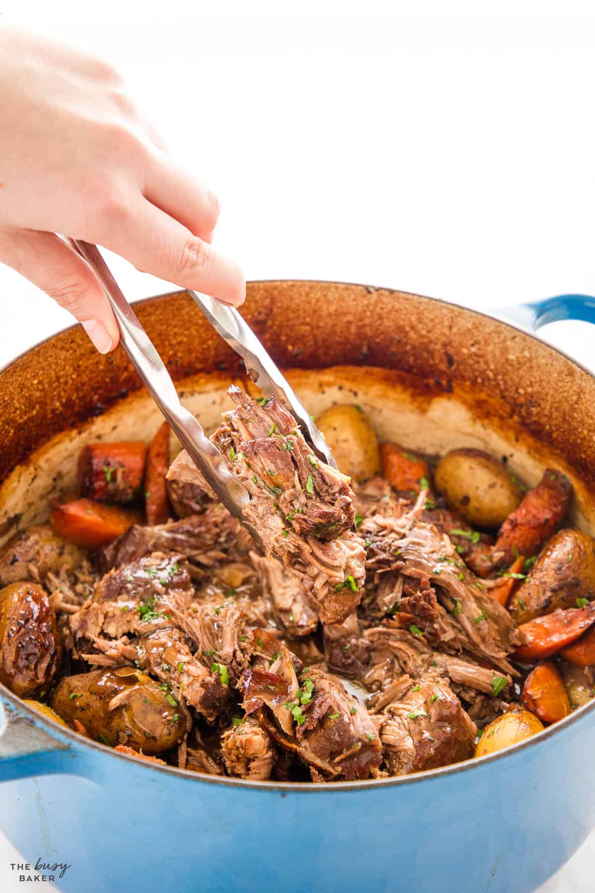 a hand using a pair of tongs to serve pot roast from a blue cast iron pot