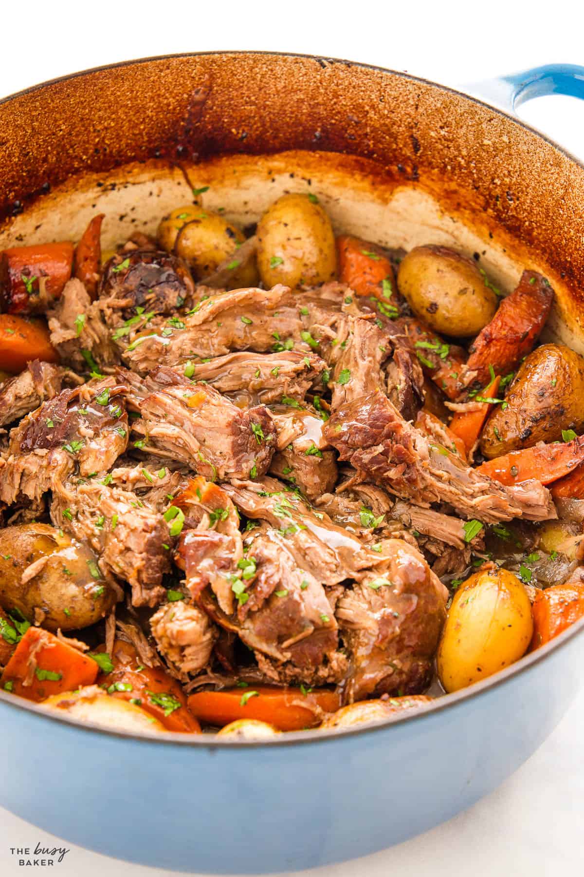 shredded beef in a dutch oven with gravy, carrots and potatoes