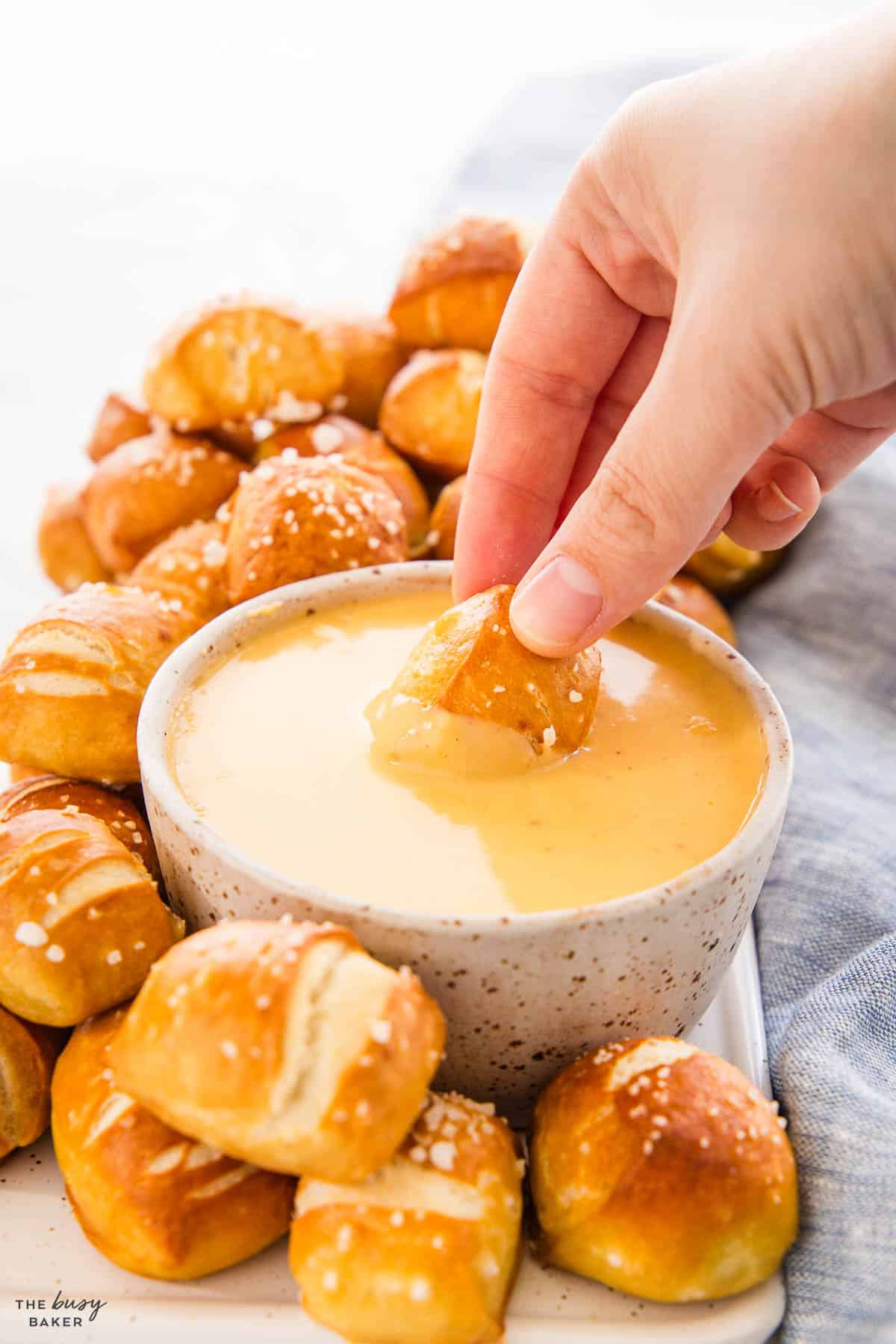 hand dipping pretzel bite into cheese sauce