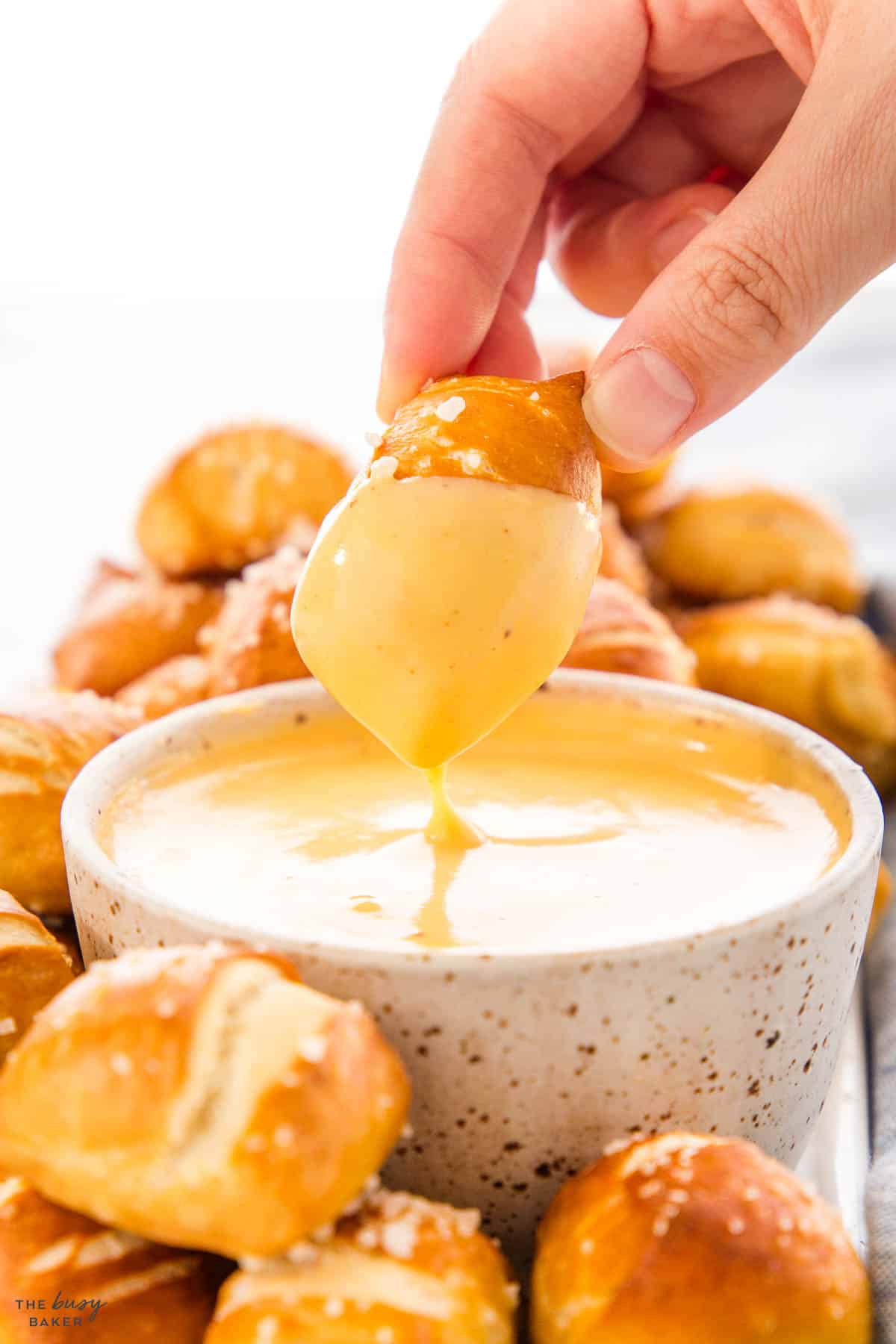 hand dipping a pretzel bite in cheese sauce