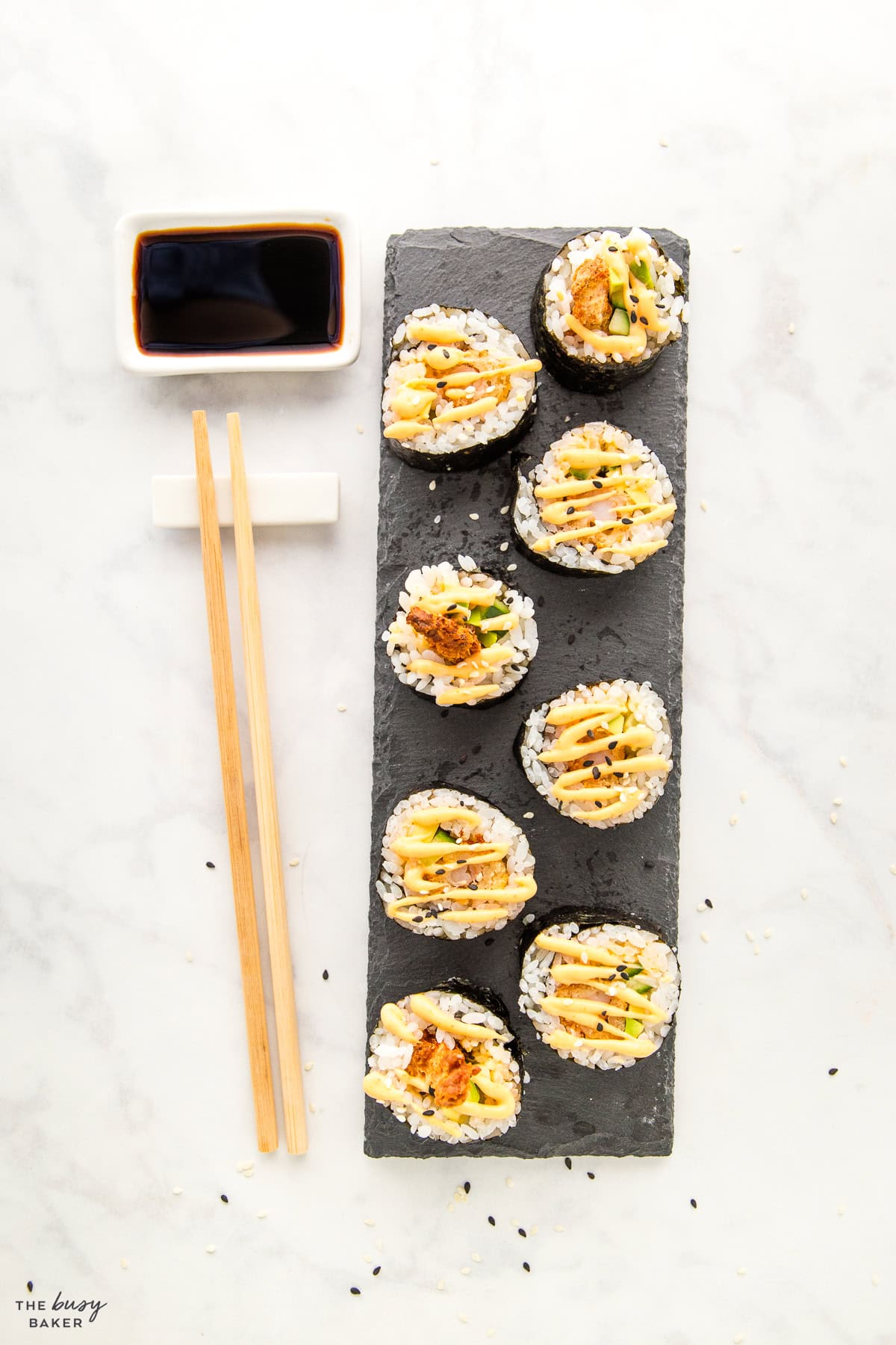 dynamite rolls on a slate board with soy sauce and chopsticks