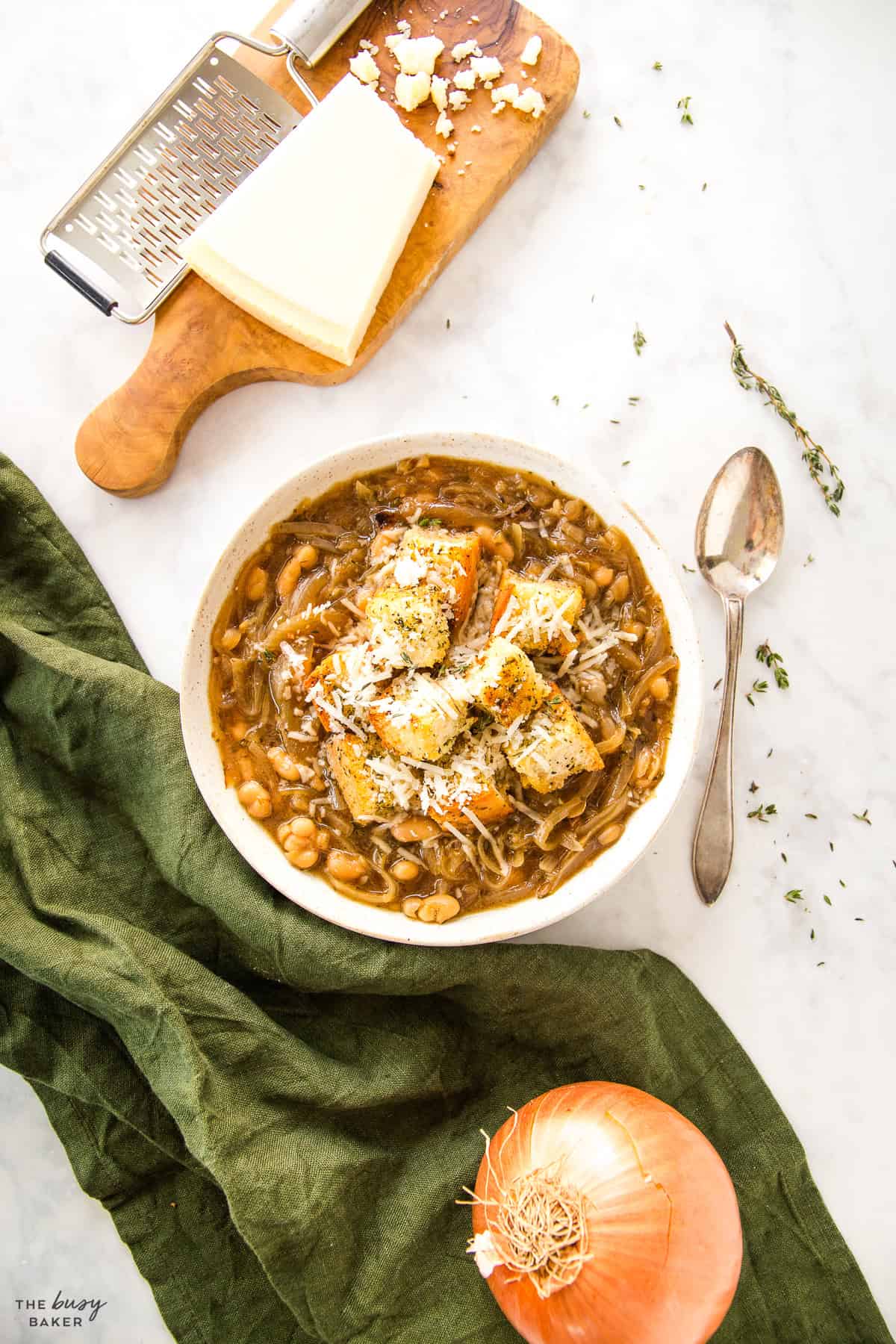 overhead image: white bean french onion soup in a bowl with croutons and Parmesan cheese