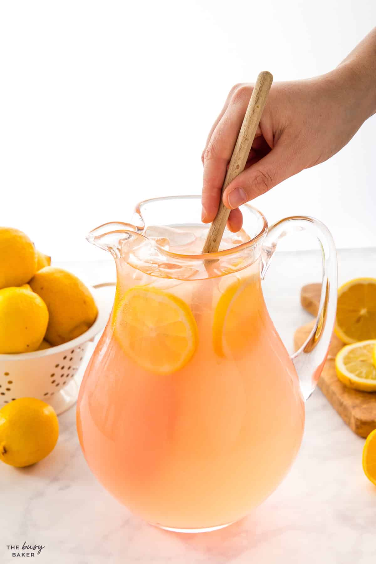 hand stirring a pitcher of lemonade with a wooden spoon