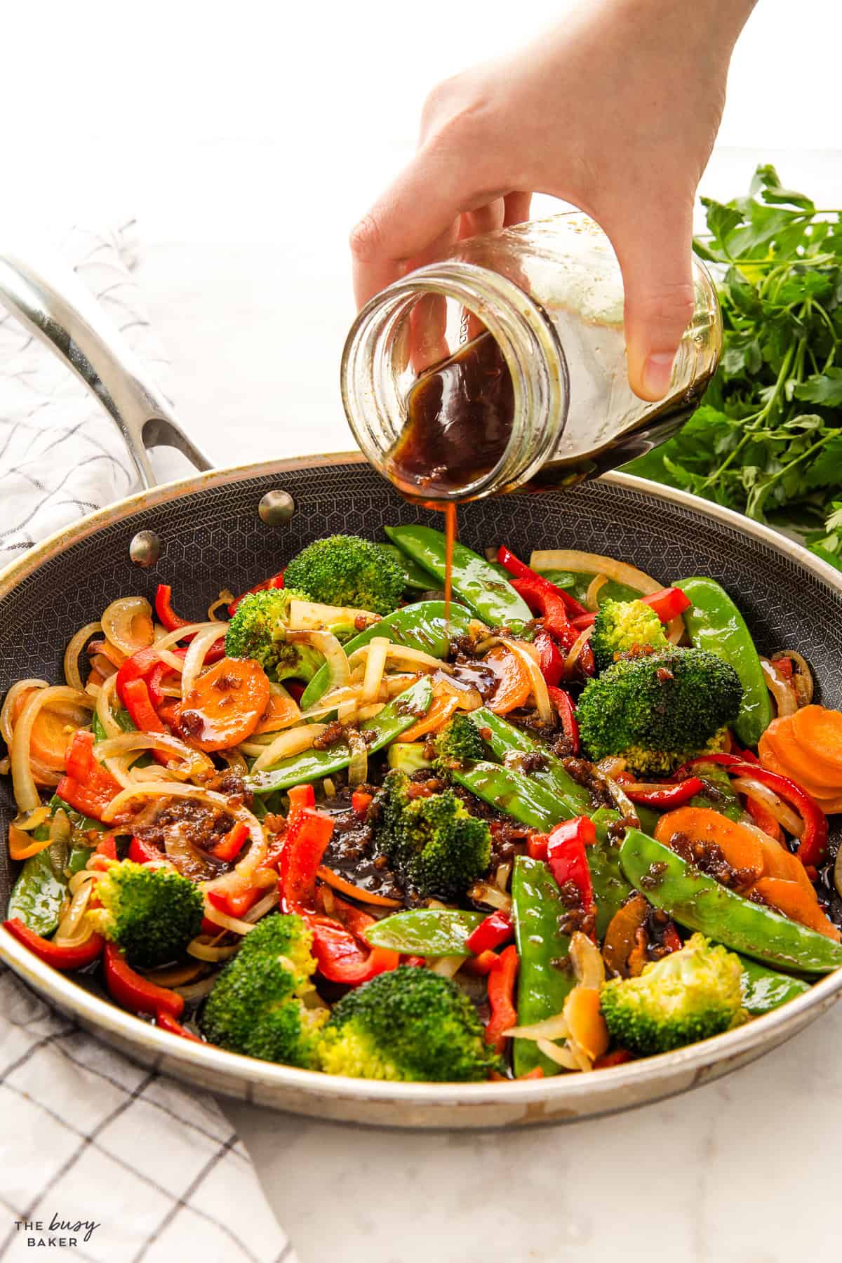 hand pouring stir fry sauce from a mason jar into a stir fry in a skillet