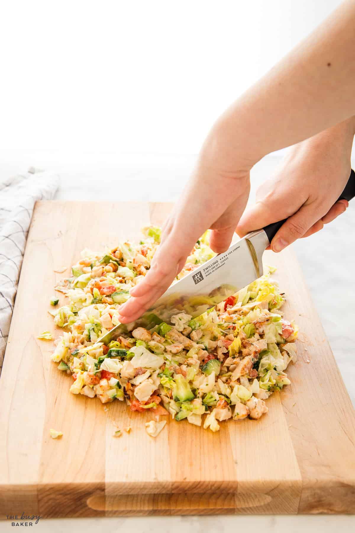 hand chopping salad on a board with a large knife