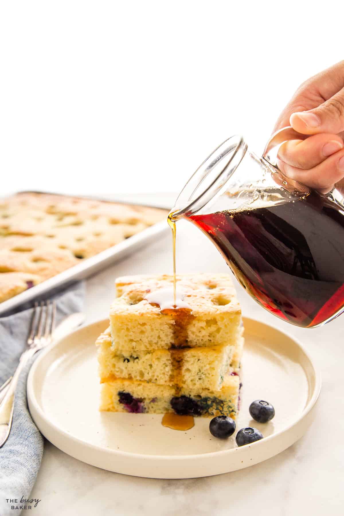hand pouring maple syrup over sheet pan pancakes