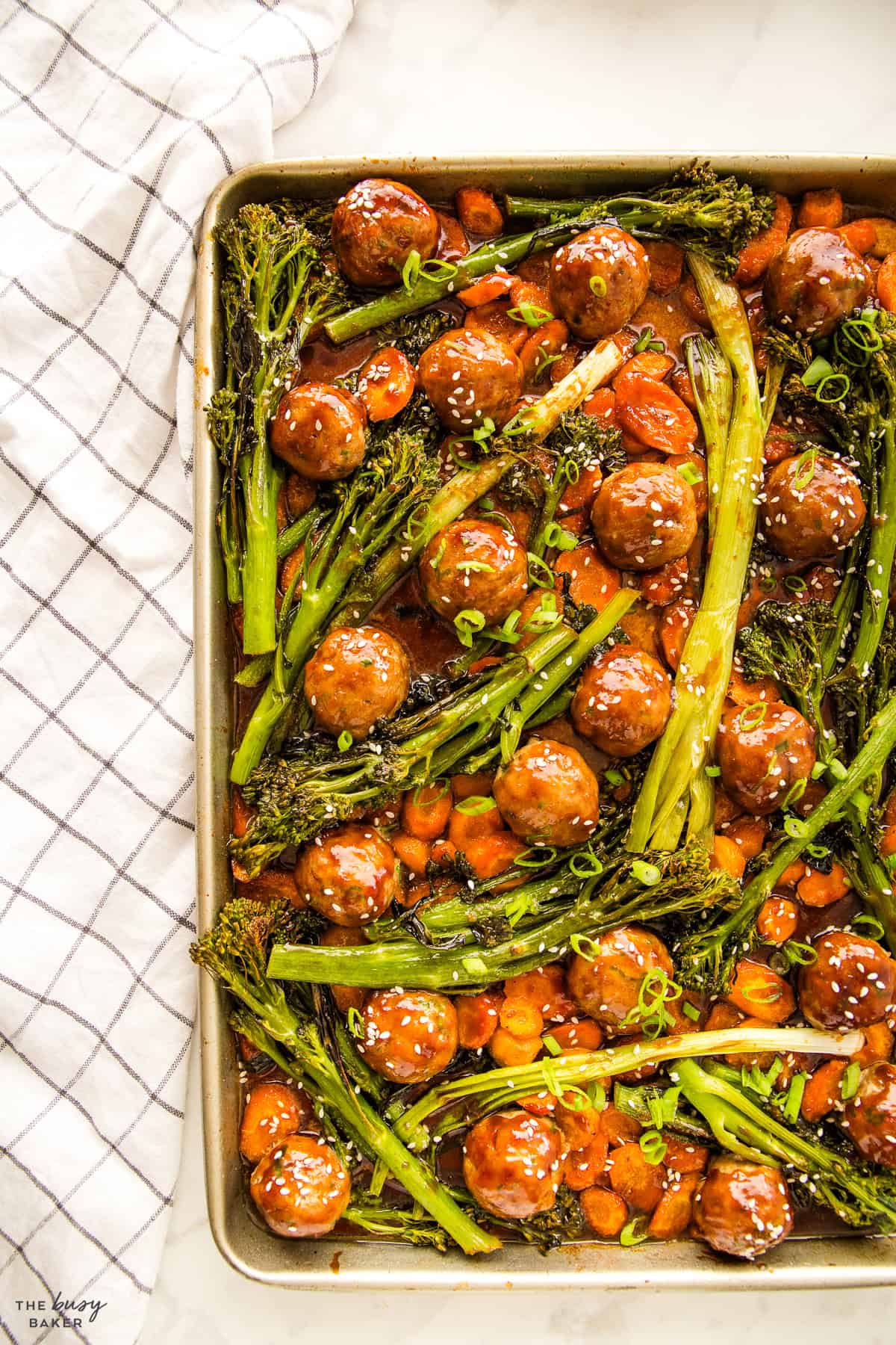 meatballs and broccolini on a sheet pan topped with teriyaki glaze and sesame seeds