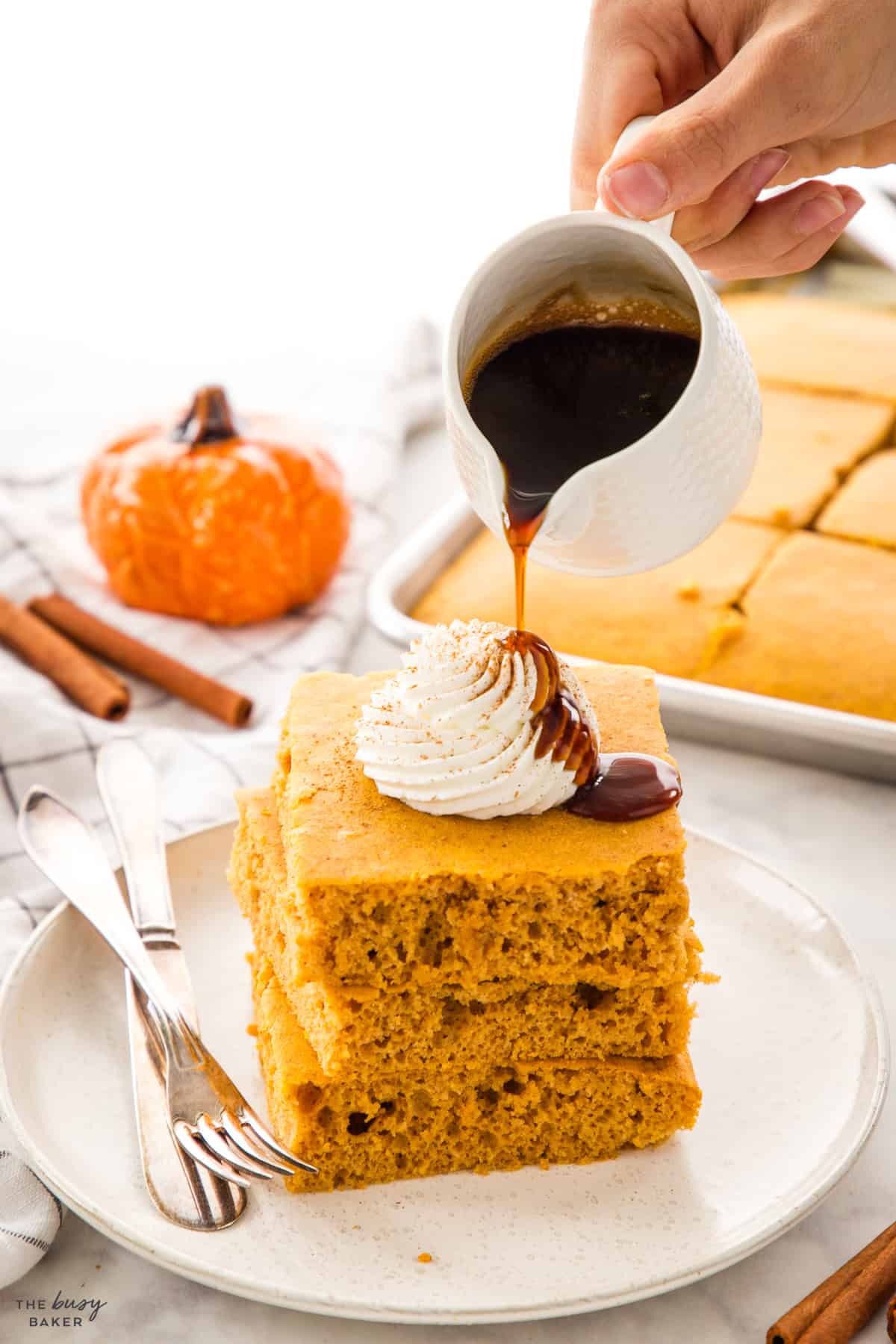 hand pouring maple syrup over a stack of sheet pan pumpkin pancakes