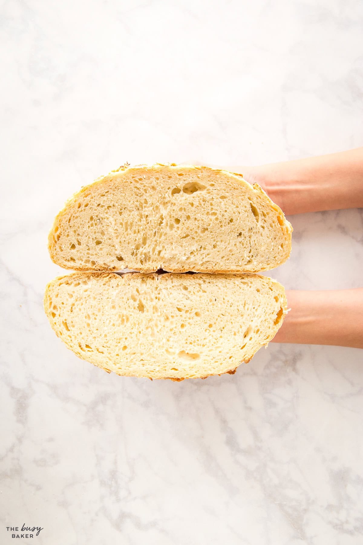 hand holding two halves of a loaf of crusty bread