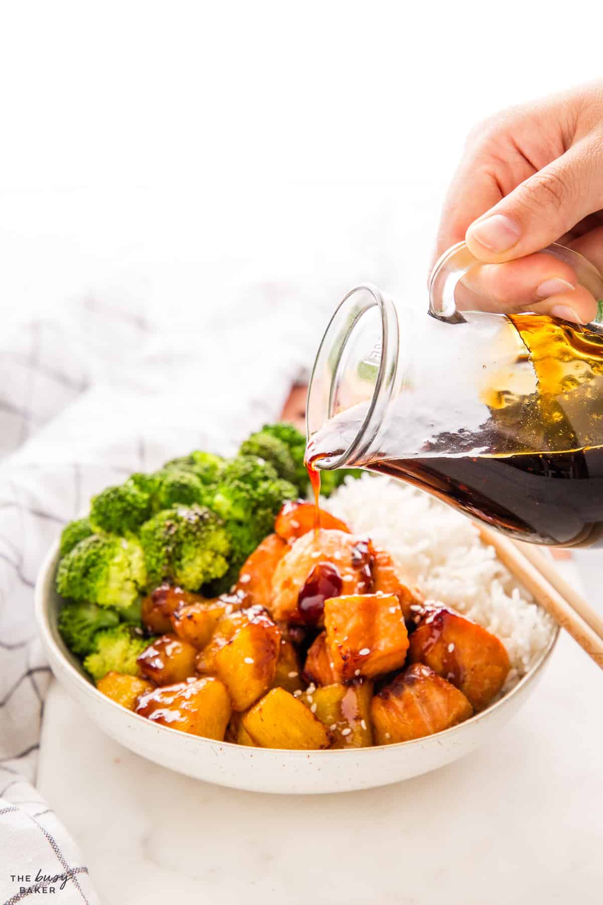 pouring teriyaki sauce over salmon, rice and broccoli