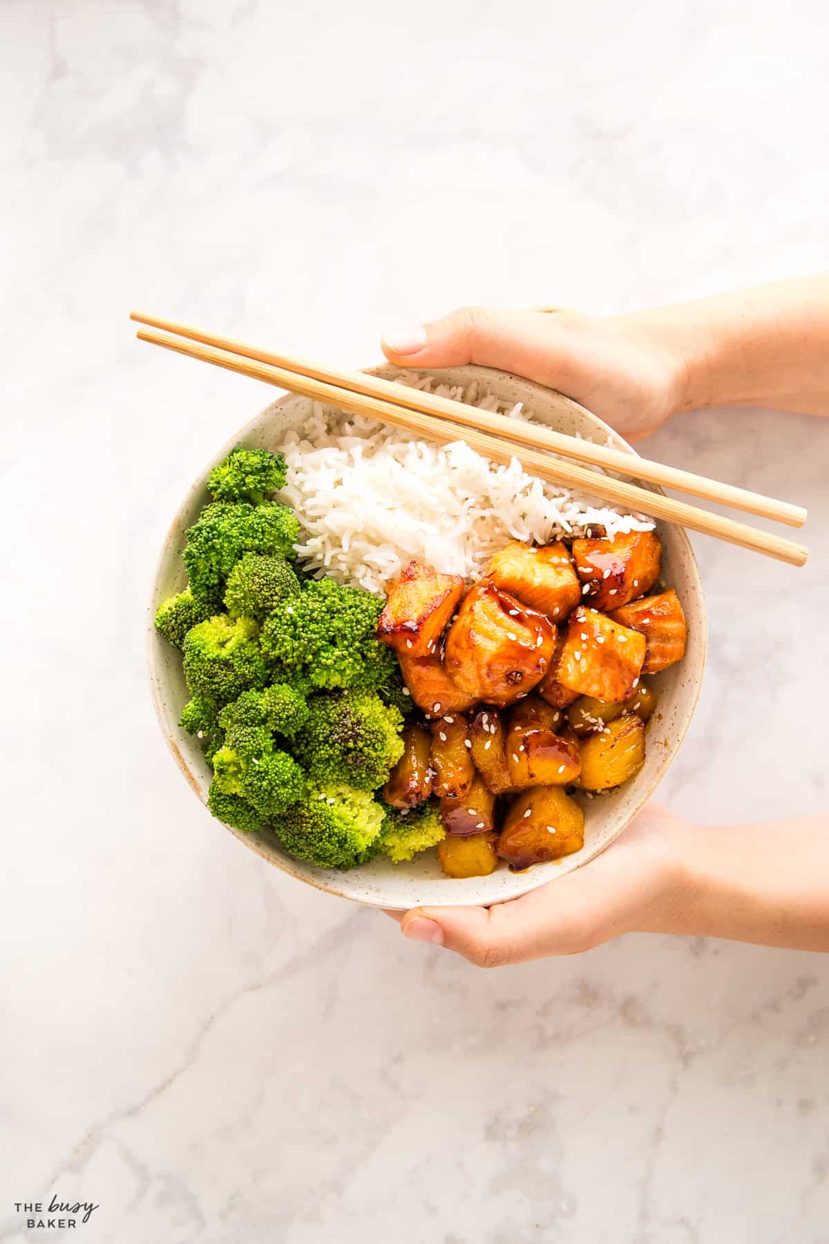 hands holding a teriyaki salmon bowl