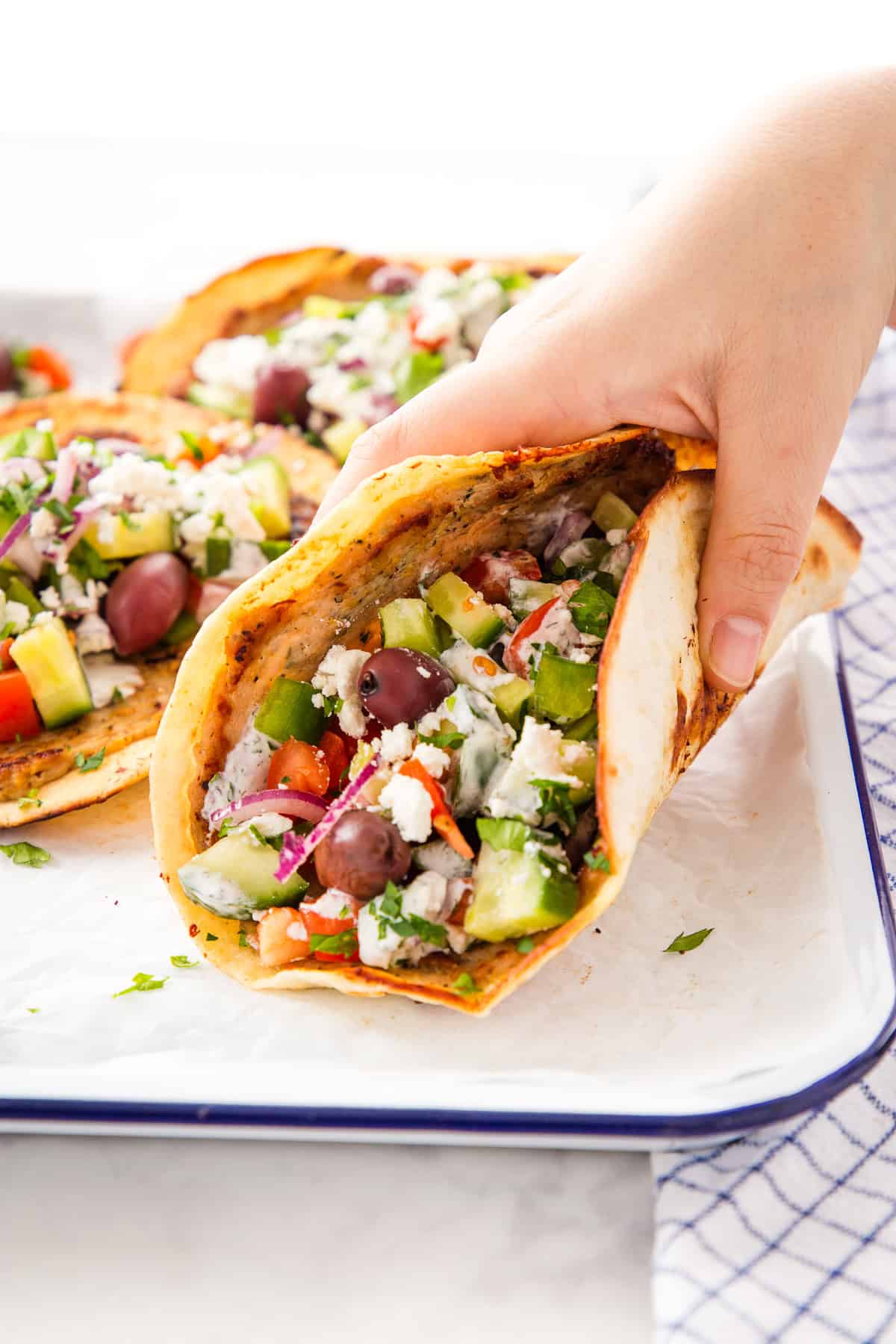 hand holding a greek-style smash taco with chicken