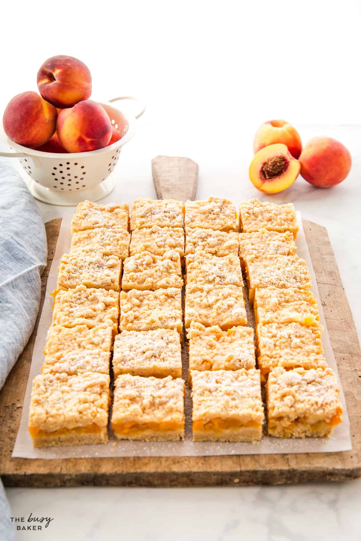 peach crumb bars cut on a wooden board with fresh peaches
