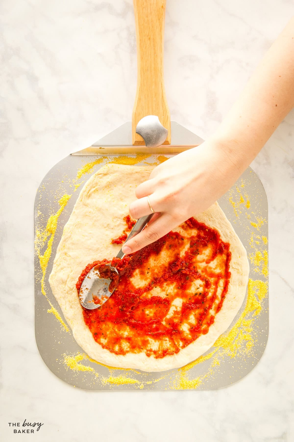 hand spreading pizza sauce onto pizza dough on a pizza peel