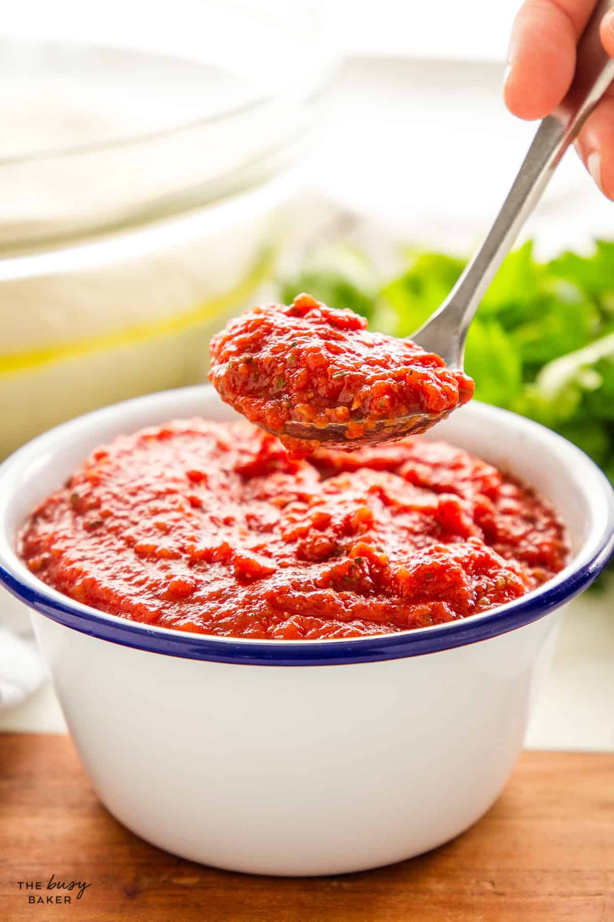 hand ladling pizza sauce out of a bowl