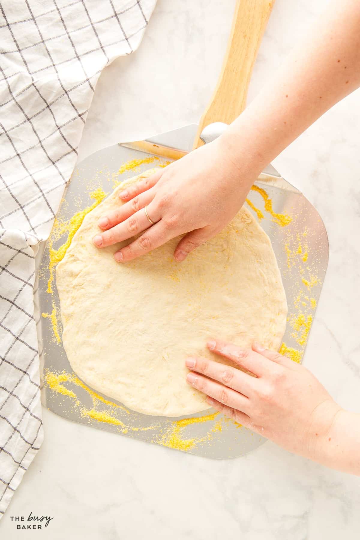hands stretching pizza dough on a metal pizza peel