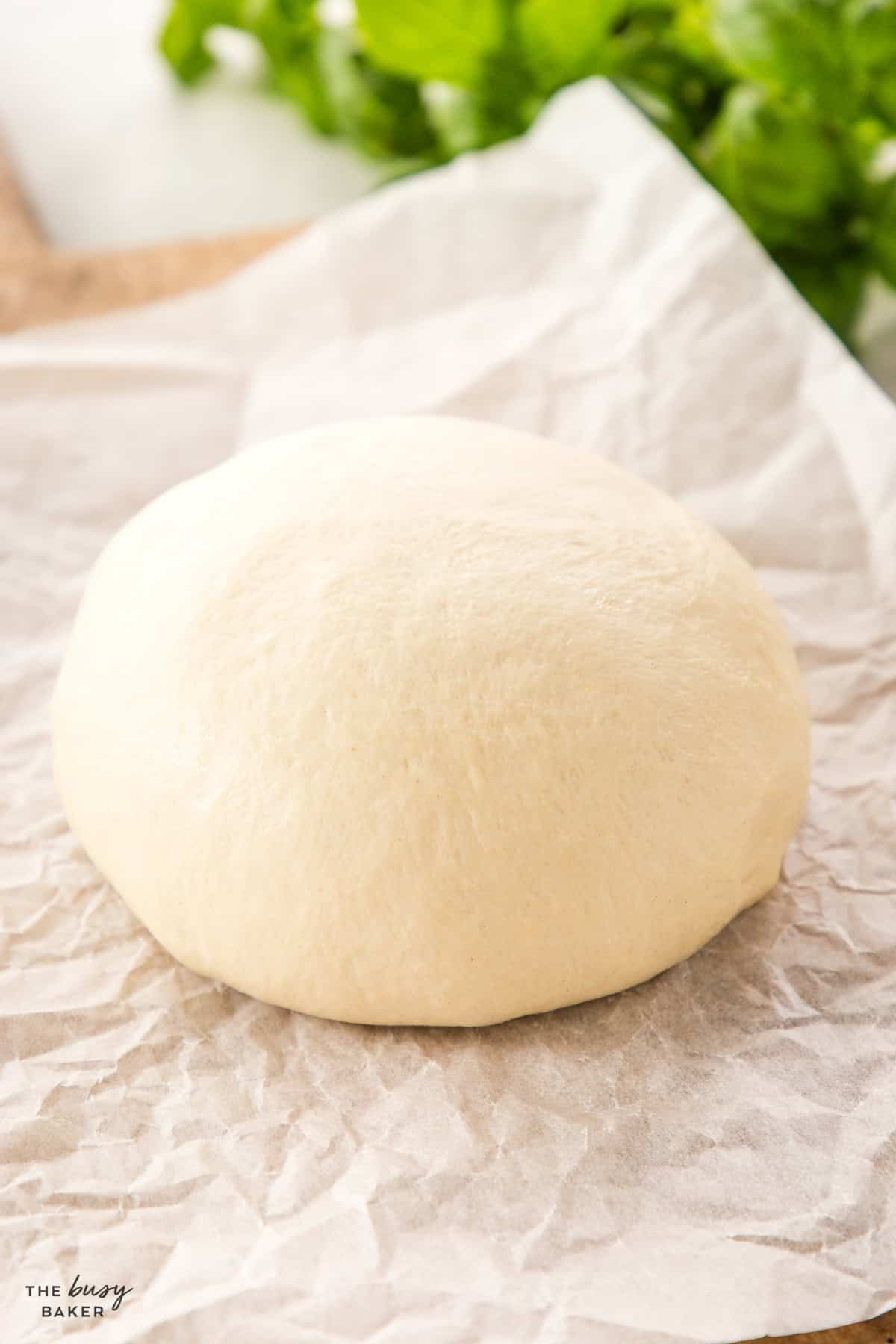 pizza dough sitting on a wooden board with parchment paper