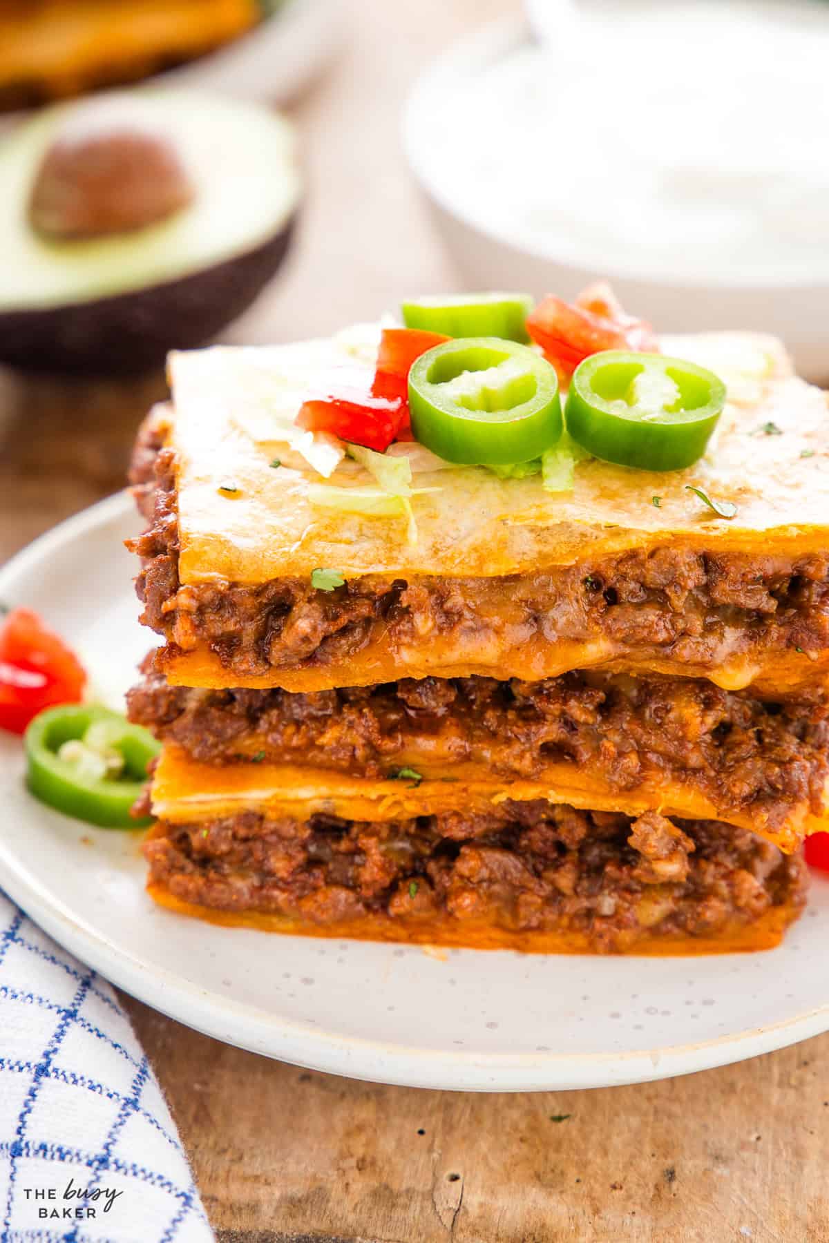 Stack of sheet pan quesadilla squares showing layers of taco meat and cheese, topped with lettuce and jalapeño