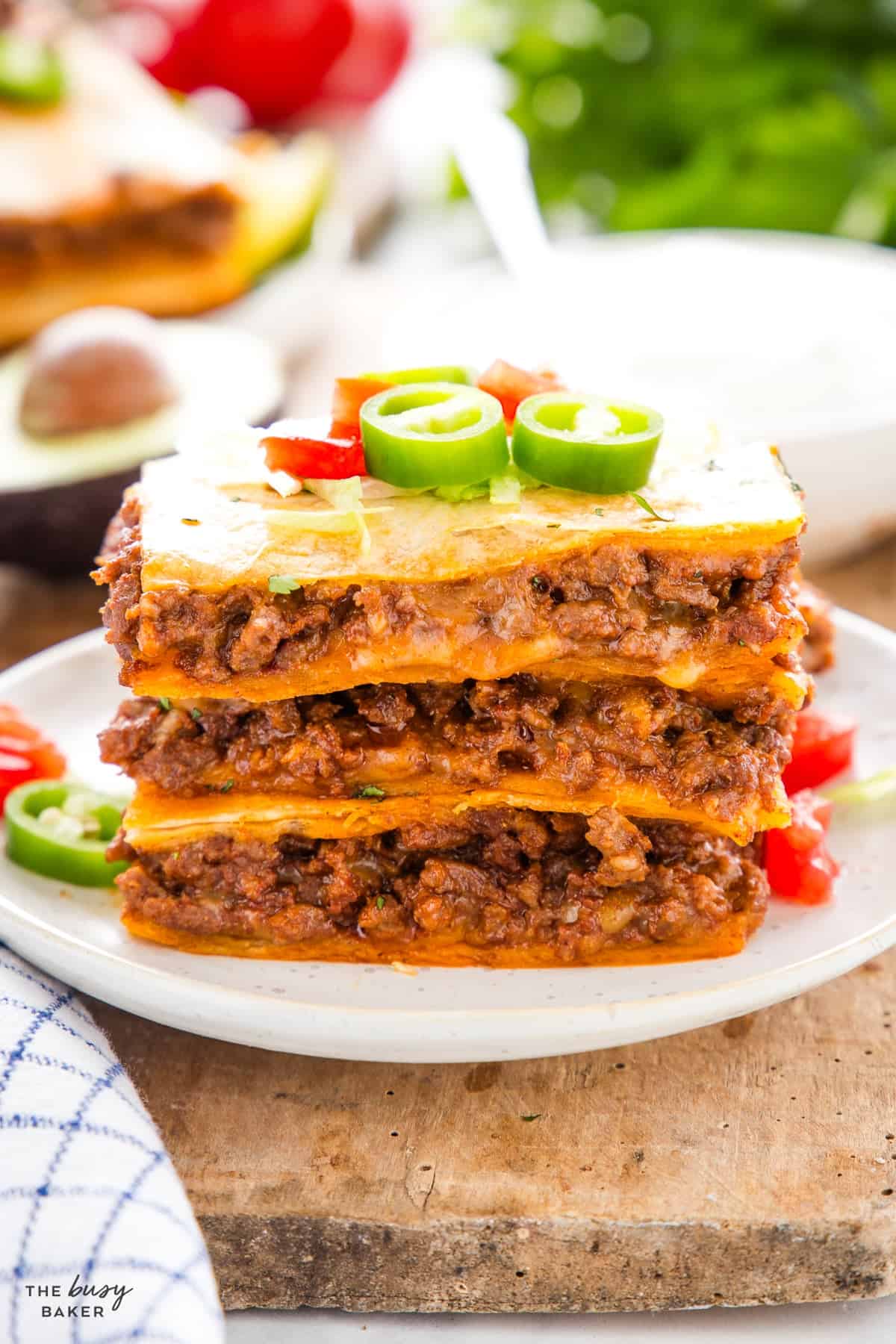 Stack of sheet pan quesadilla squares showing layers of taco meat and cheese, topped with lettuce and jalapeño