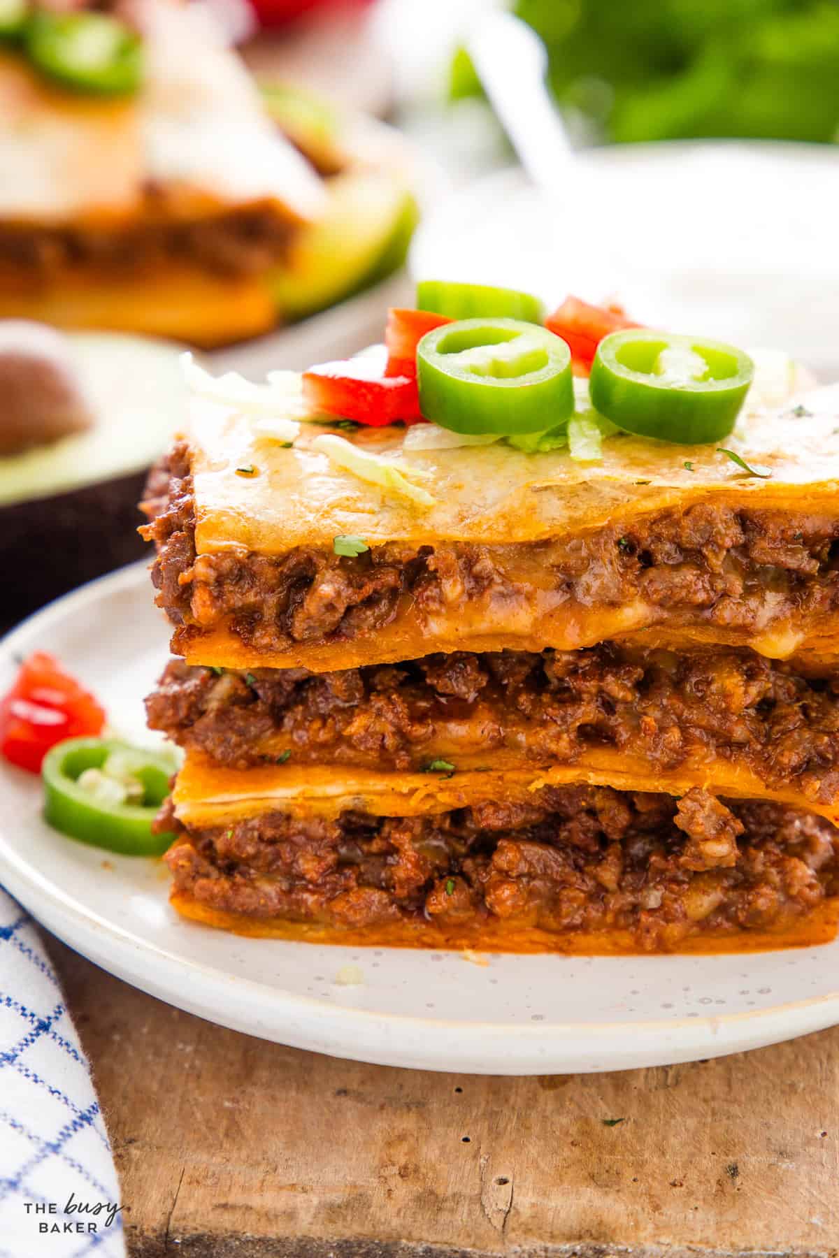Stack of sheet pan quesadilla squares showing layers of taco meat and cheese, topped with lettuce and jalapeño