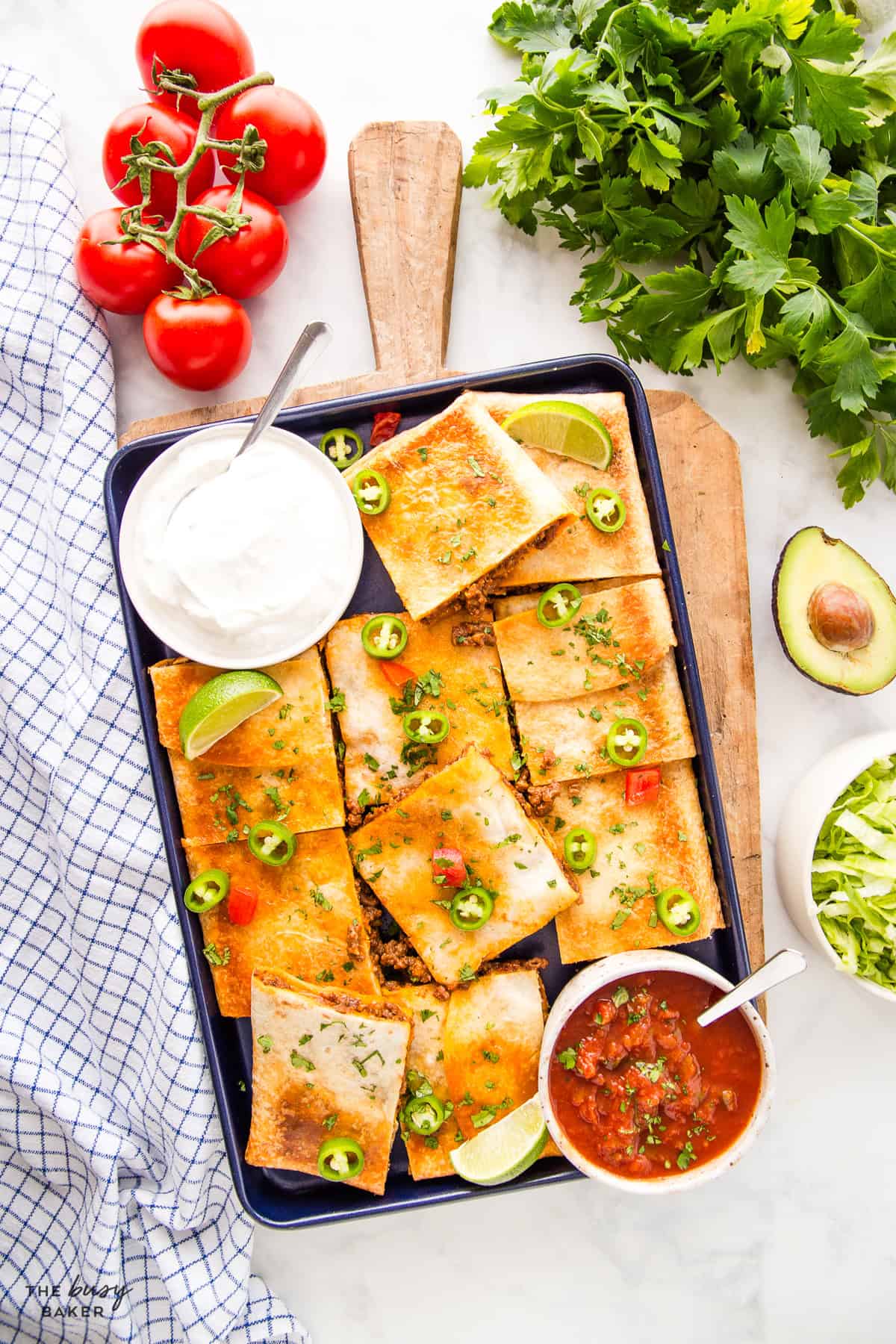 Sheet pan quesadillas cut into squares on a baking sheet with sour cream, salsa, and avocado