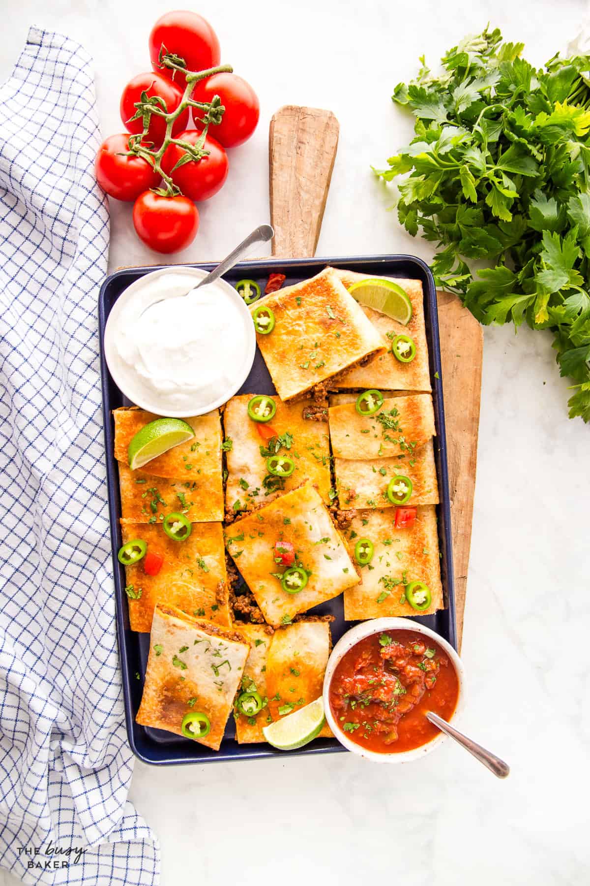 Sheet pan quesadillas cut into squares on a baking sheet with sour cream, salsa, and avocado