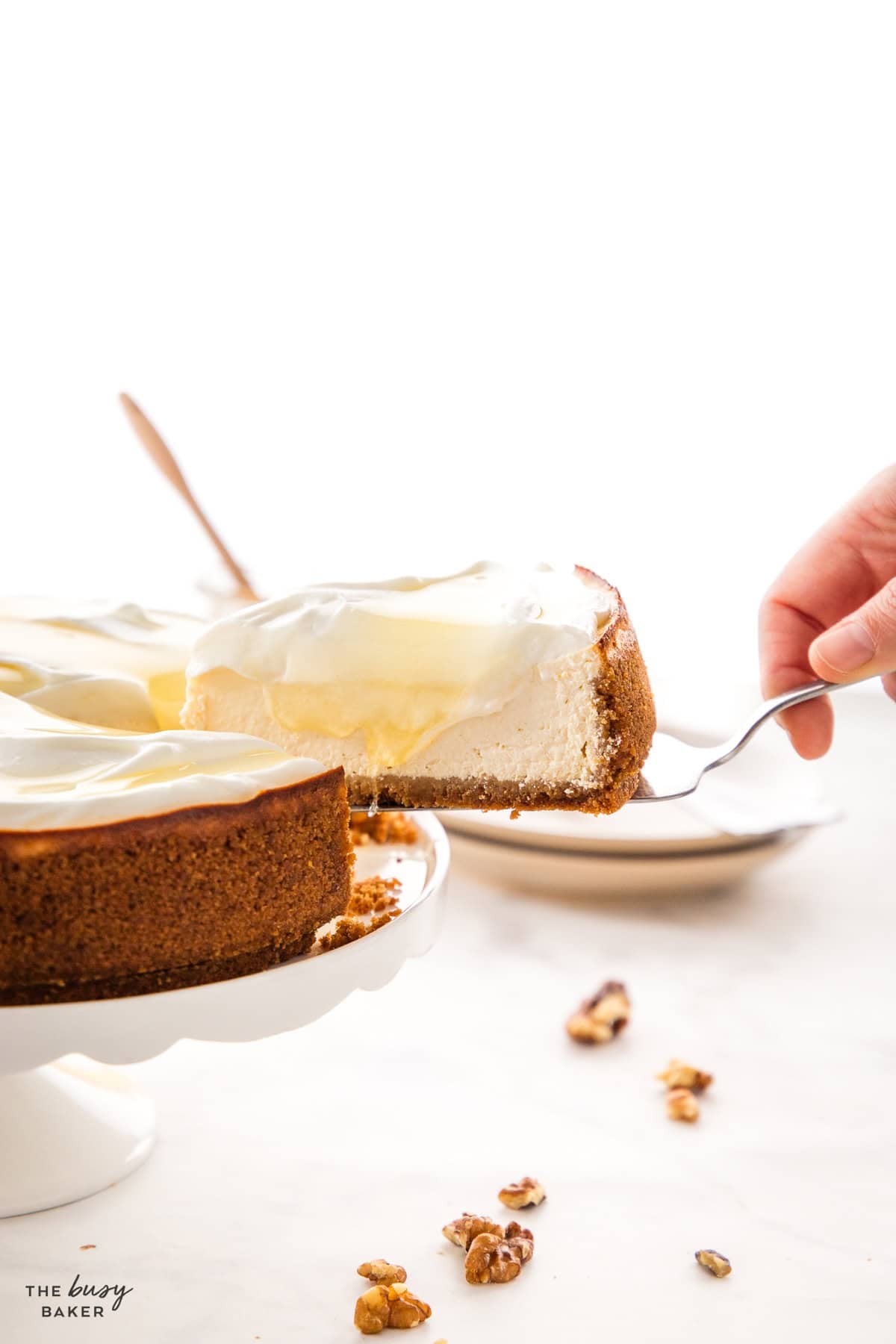 Healthy Greek yogurt cheesecake topped with whipped cream, honey, and walnuts on a white cake stand