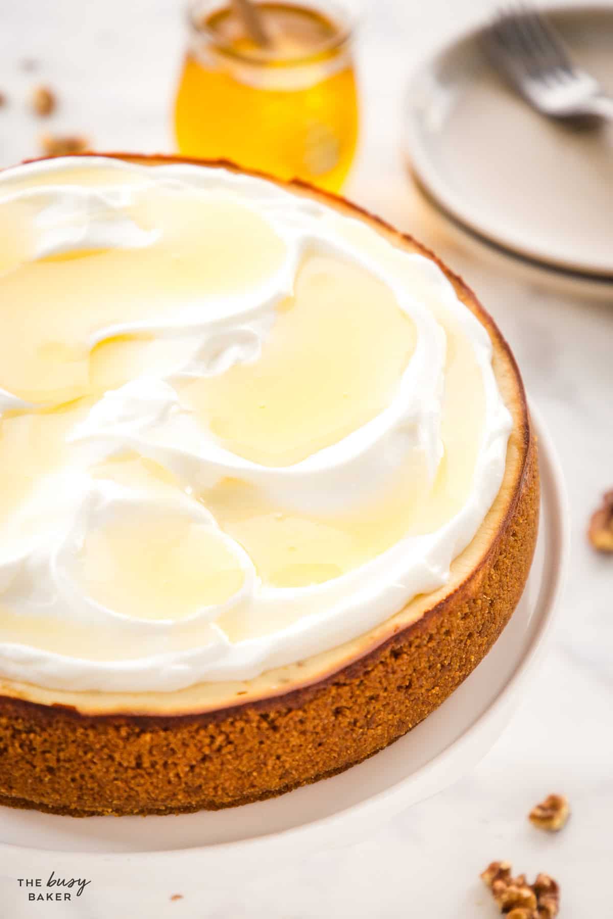 Healthy Greek yogurt cheesecake topped with whipped cream, honey, and walnuts on a white cake stand