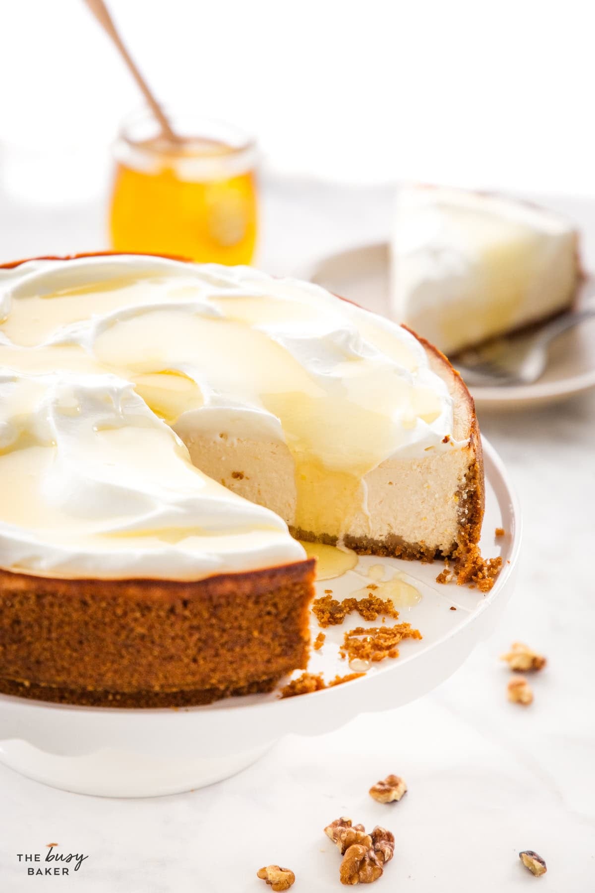 Healthy Greek yogurt cheesecake topped with whipped cream, honey, and walnuts on a white cake stand