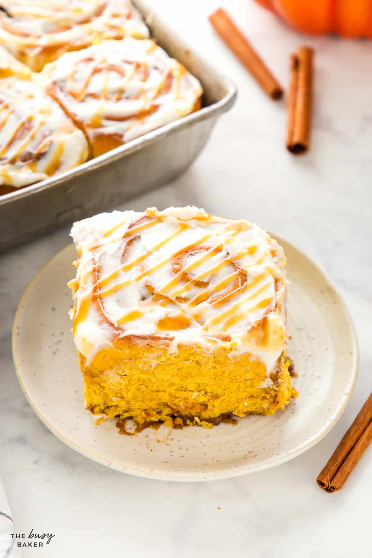 One pumpkin cinnamon roll on a plate with cream cheese glaze and fluffy interior