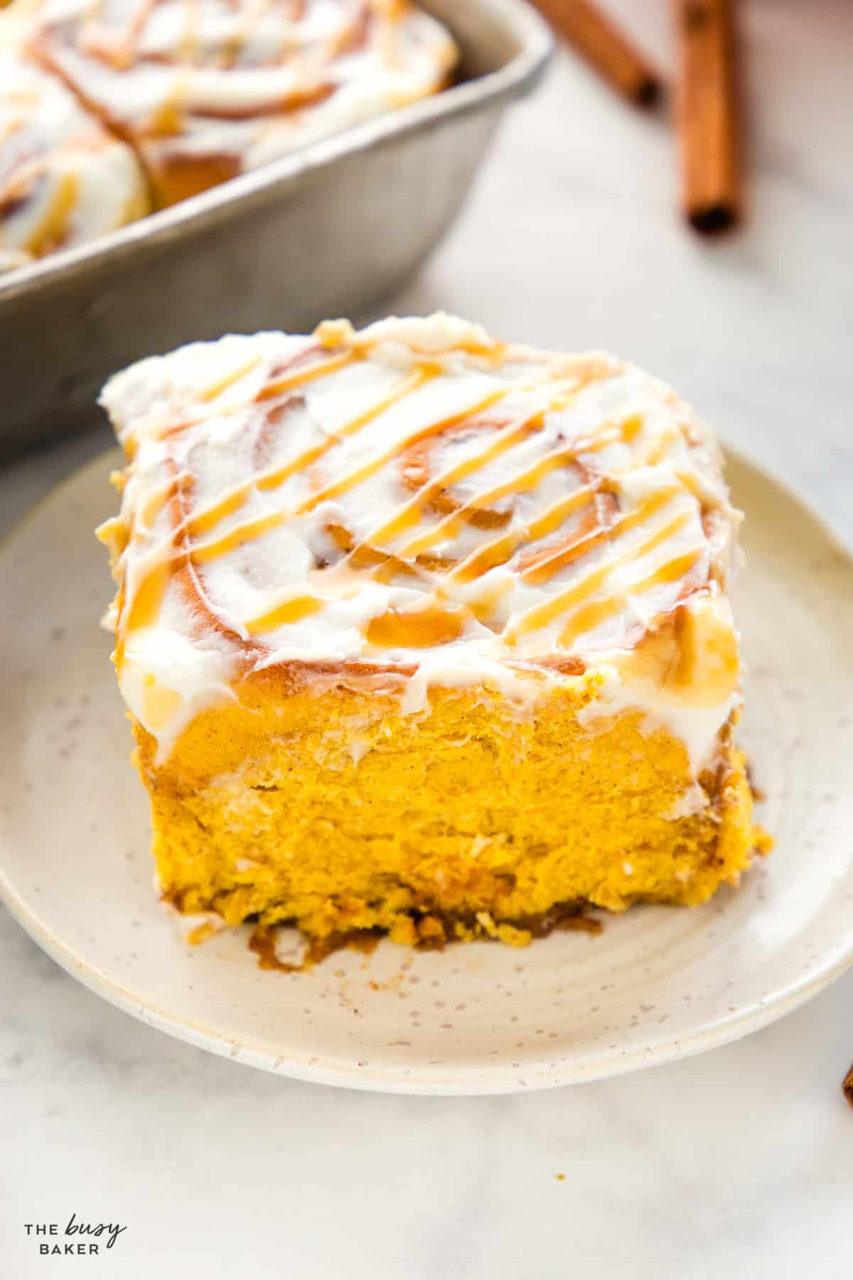 One pumpkin cinnamon roll on a plate with cream cheese glaze and fluffy interior
