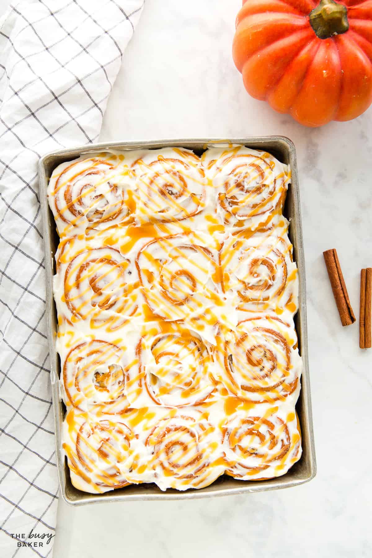 Pan of 12 pumpkin cinnamon rolls in a 9x13 baking dish with cream cheese glaze and caramel drizzle
