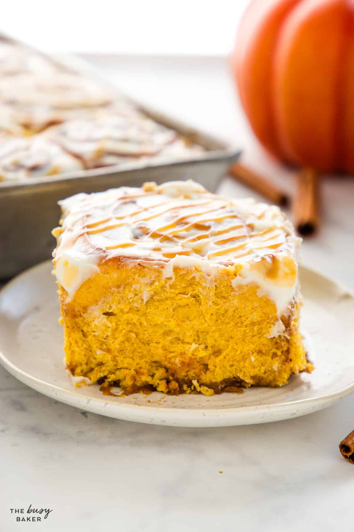 One pumpkin cinnamon roll on a plate with cream cheese glaze and fluffy interior